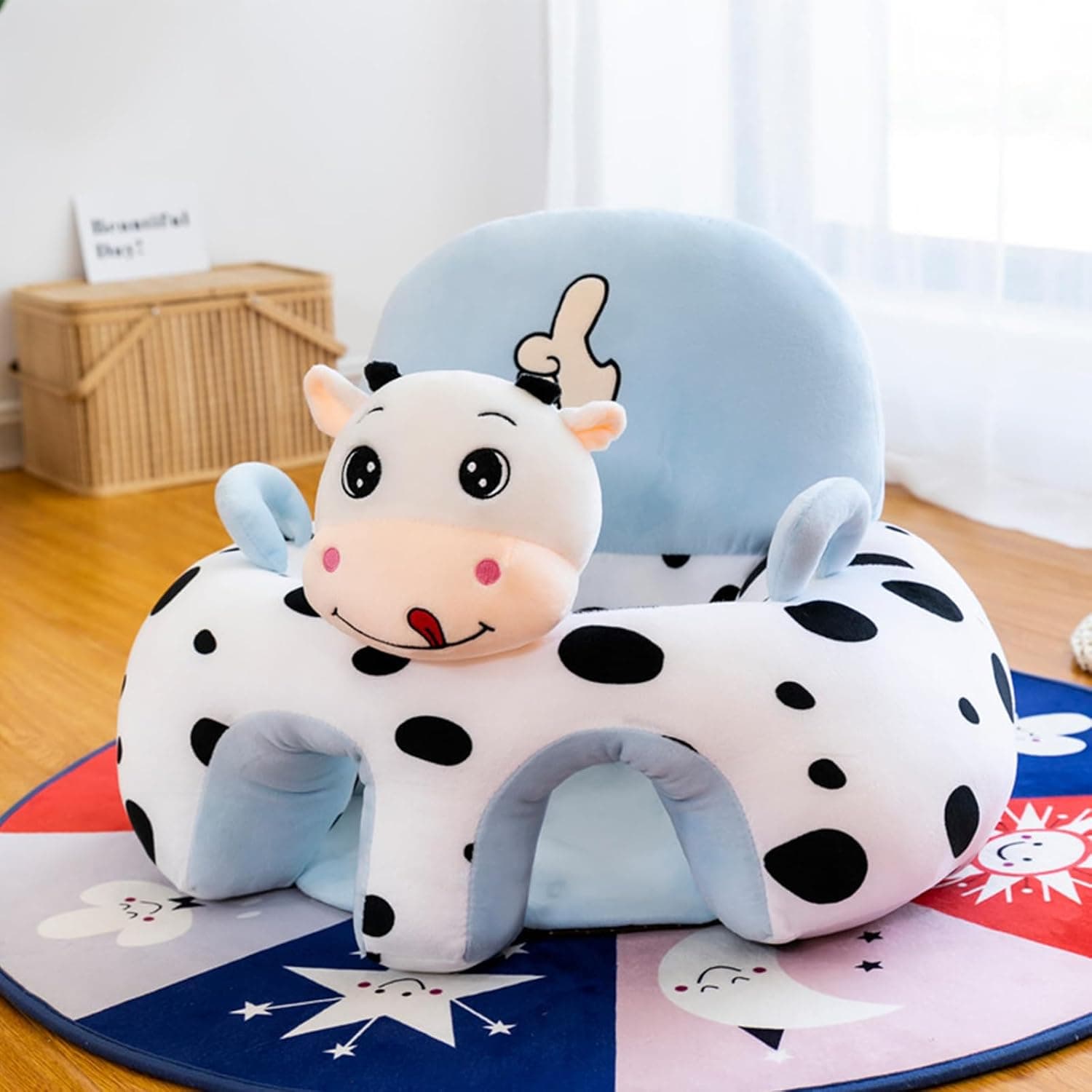 A plush blue and white cow-patterned baby floor seat sitting on a colorful star rug indoors.