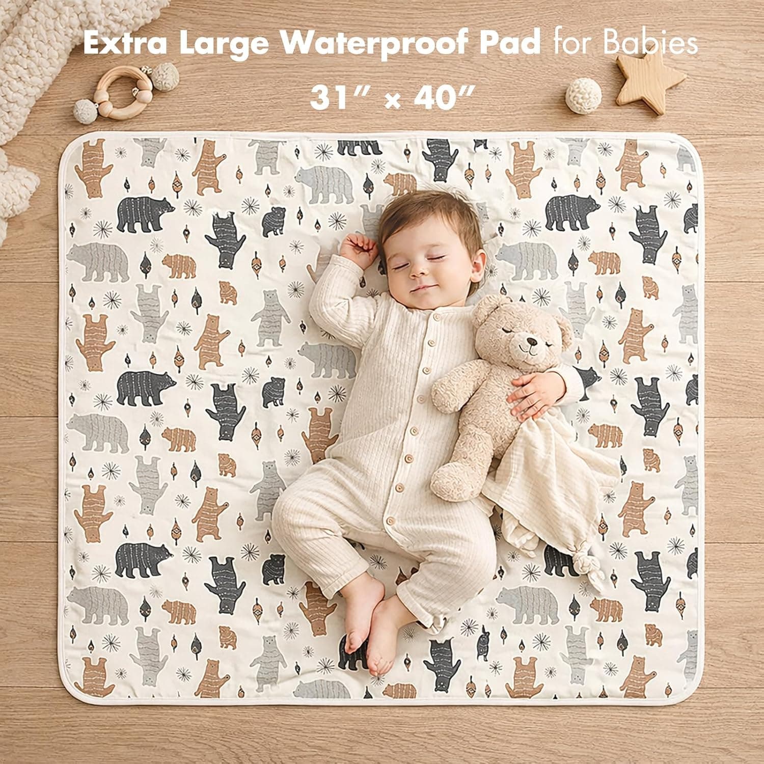 A baby sleeping peacefully on a white pad decorated with bear graphics while holding a plush teddy bear.